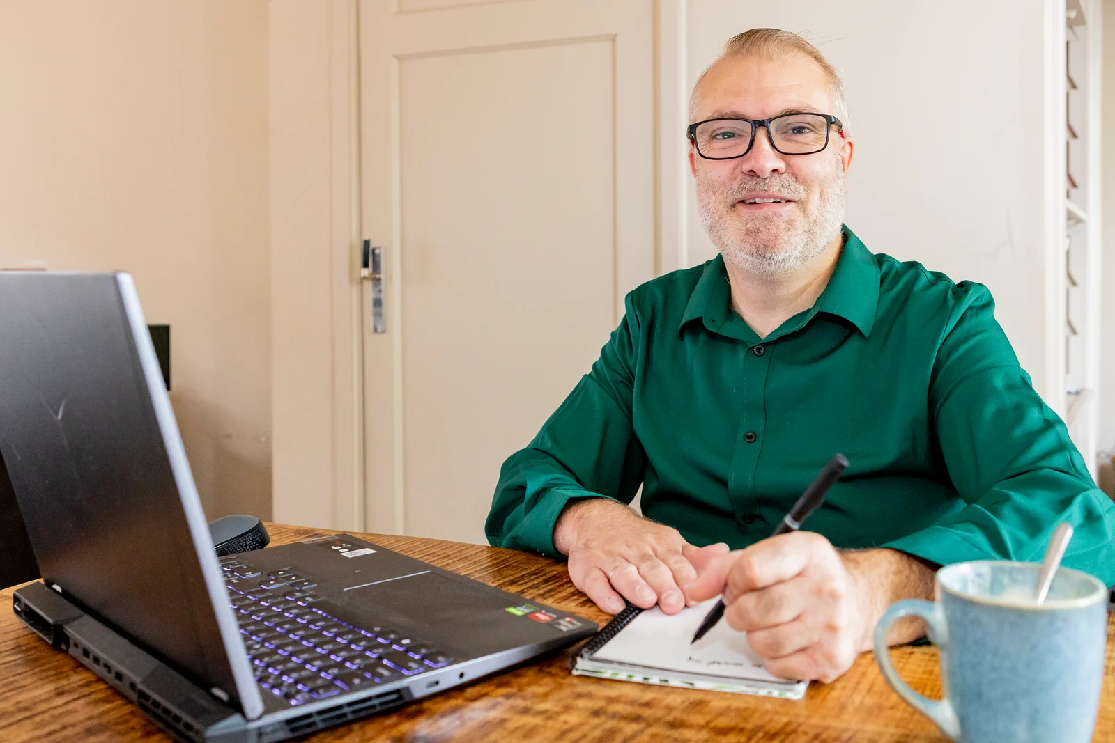 Johan schrijft bij zijn laptop en kijkt in de camera